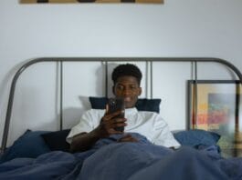 Cyfrowe nawyki, które psują sen i zdrowie psychiczne, oraz jak je zmienić Młody mężczyzna w łóżku przegląda smartfon przed snem