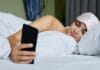 Higiena cyfrowa dla zdrowia ogólnego ile ekranów to za dużo i jak ograniczyć ich wpływ na sen Kobieta w łóżku z opaską na oczach przegląda smartfon przed snem